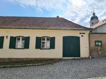 Außenansicht älteres Gebäude, pastellgelbe Fassade mit grüner Holztür und weiße Holzfenster mit grünen Fensterläden aus Holz